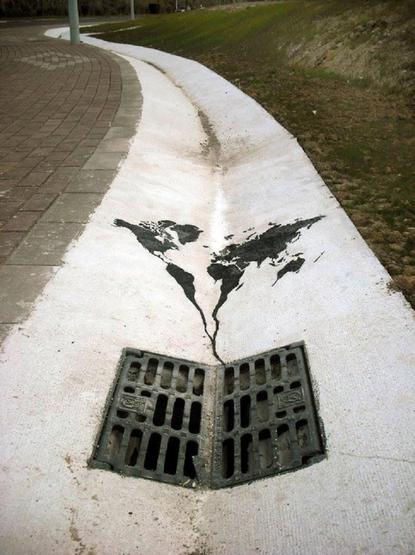 Environmental street art by Pejac in Santander, Spain: a painted black world map narrows into a stream that runs into a real street drain grate on a white curb.