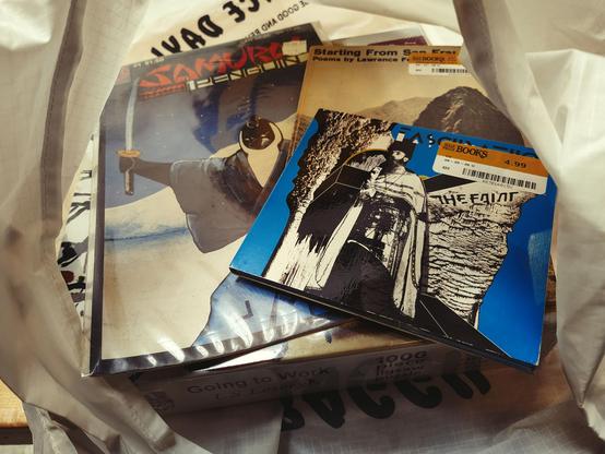 A copy of a SAMURAI PENGUIN comic book, a slim 1967 volume of Lawrence Ferlenghetti's poetry and a copy of THE FAINT's Fascination album on top of a sealed 1000 piece LS Lowry puzzle.