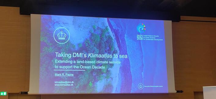 A blue slide showimg an aerial image of the coast announcing the talk Taking DMI's Klimaatlas to sea