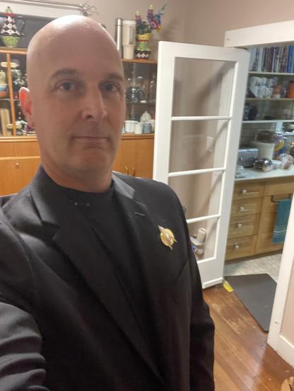 I am standing in my dining room with black jacket on and a black turtleneck. Over the jacket is a Star Trek pin. There are 4 dark pipe shining on my turtleneck