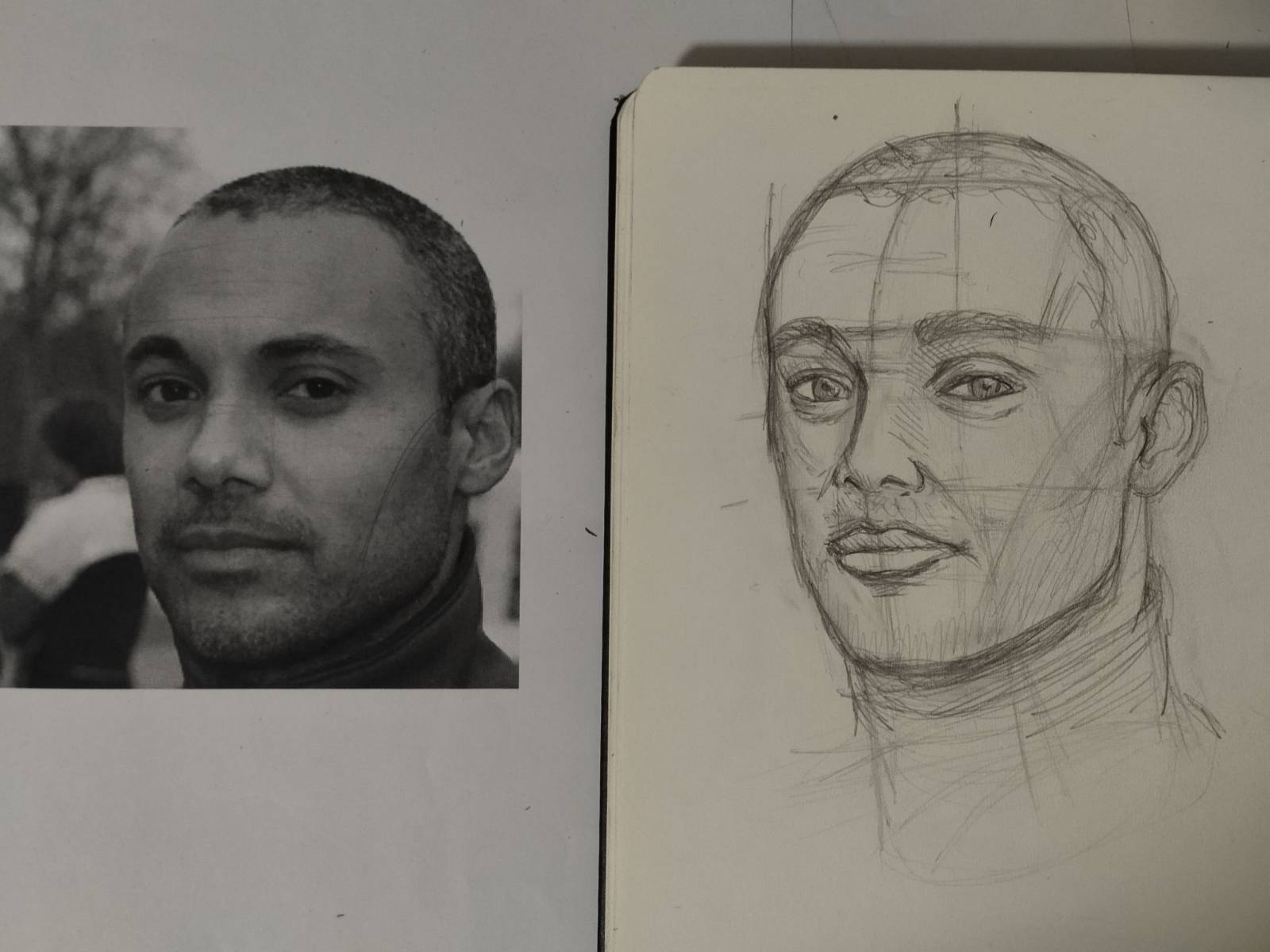 Picture and drawing of a man's face. On the left is the pictures, black and white. And on the right is a drawing of on a sketchbook page. The man has a slight smile, very short hair, a slightly trimmed beard, both dark and looking at the camera. The drawing has some guiding lines/curves and no shadows/values.